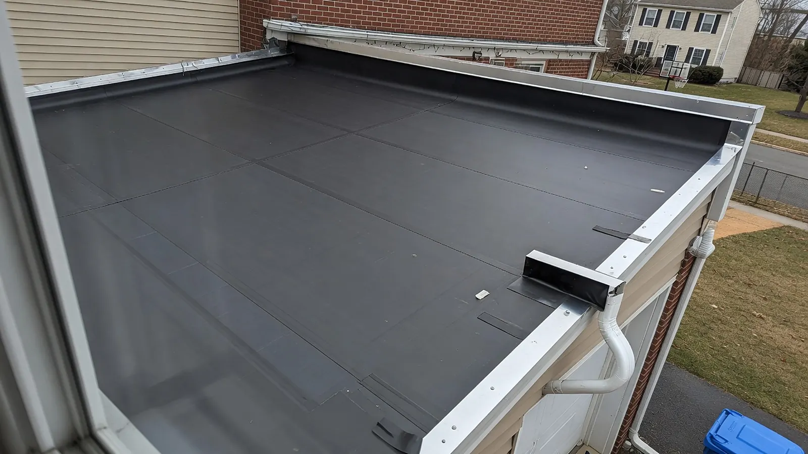 Low-slope roof over an attached garage covered in a new black membrane with clean seams and aluminum edge trim