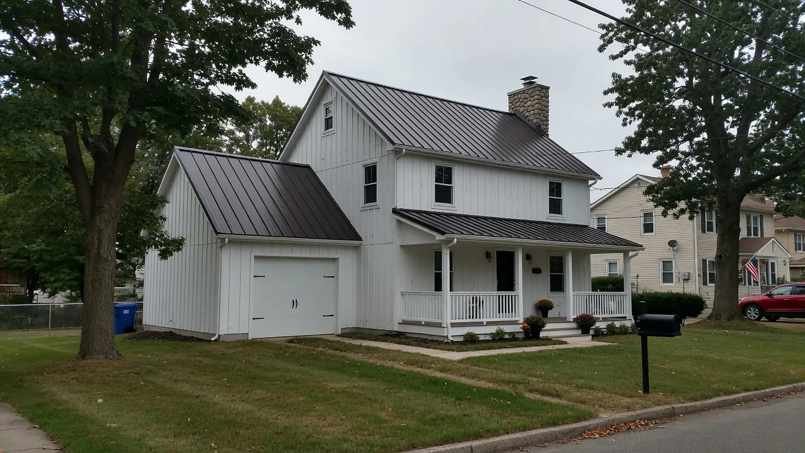 White farmhouse-style home with a dark bronze standing seam metal roof and a stone chimney