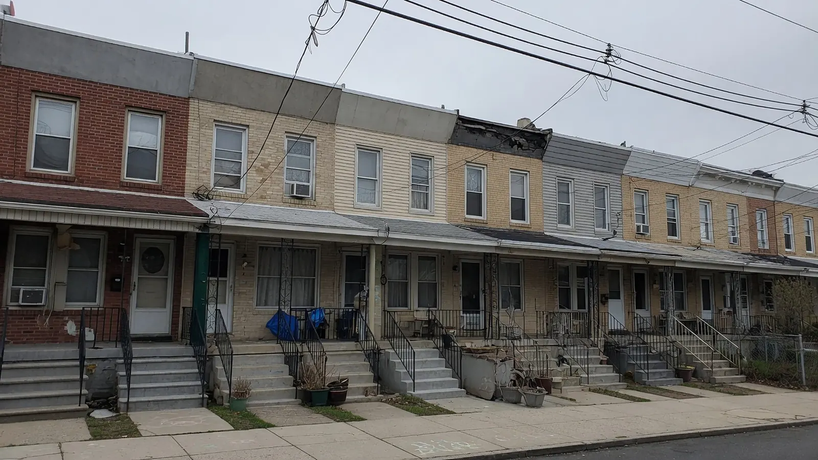 North Bergen-style block of attached flat-roof row houses with front stoops, one with a damaged cornice