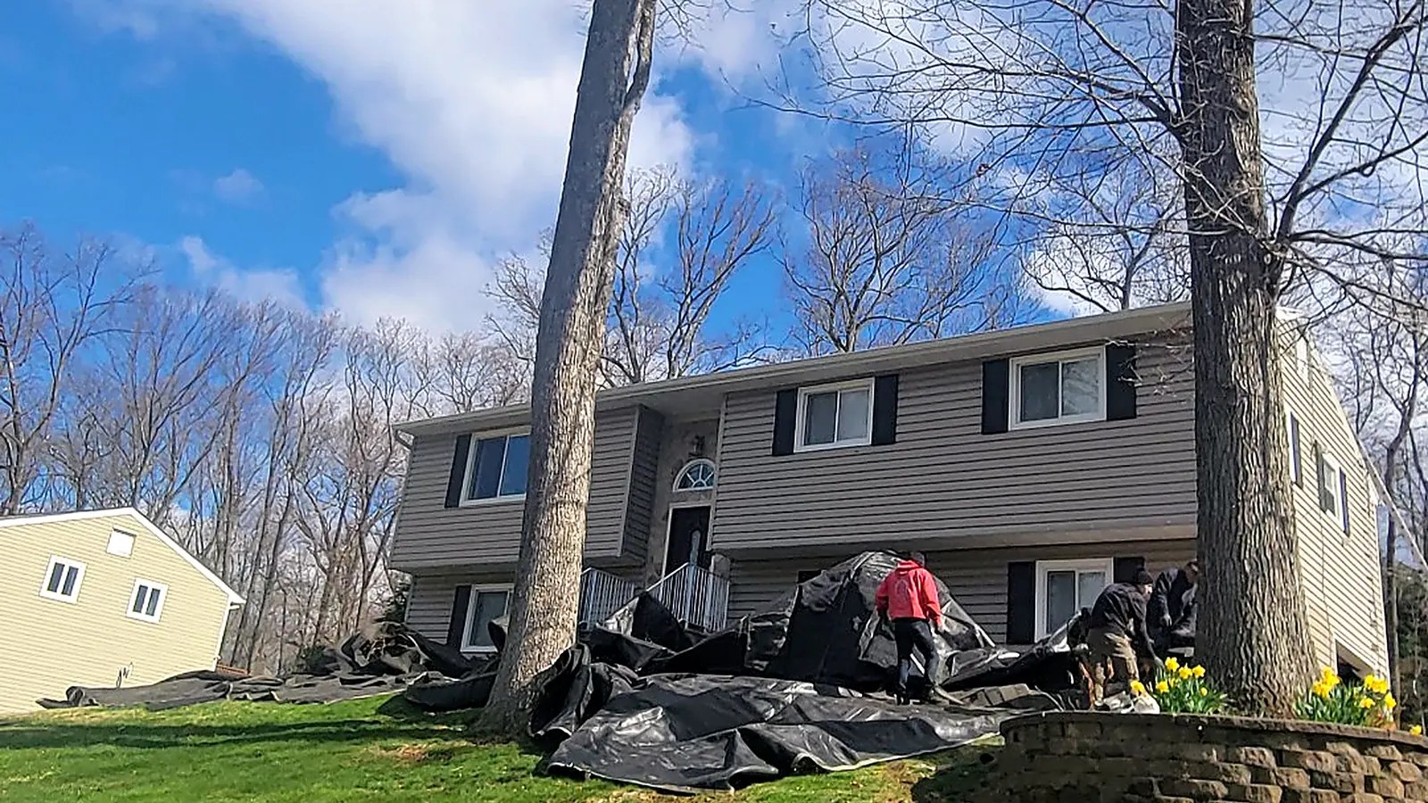 RJ Construction crew spreading black tarps around a raised ranch to protect the lawn and shrubs before a roof tear-off