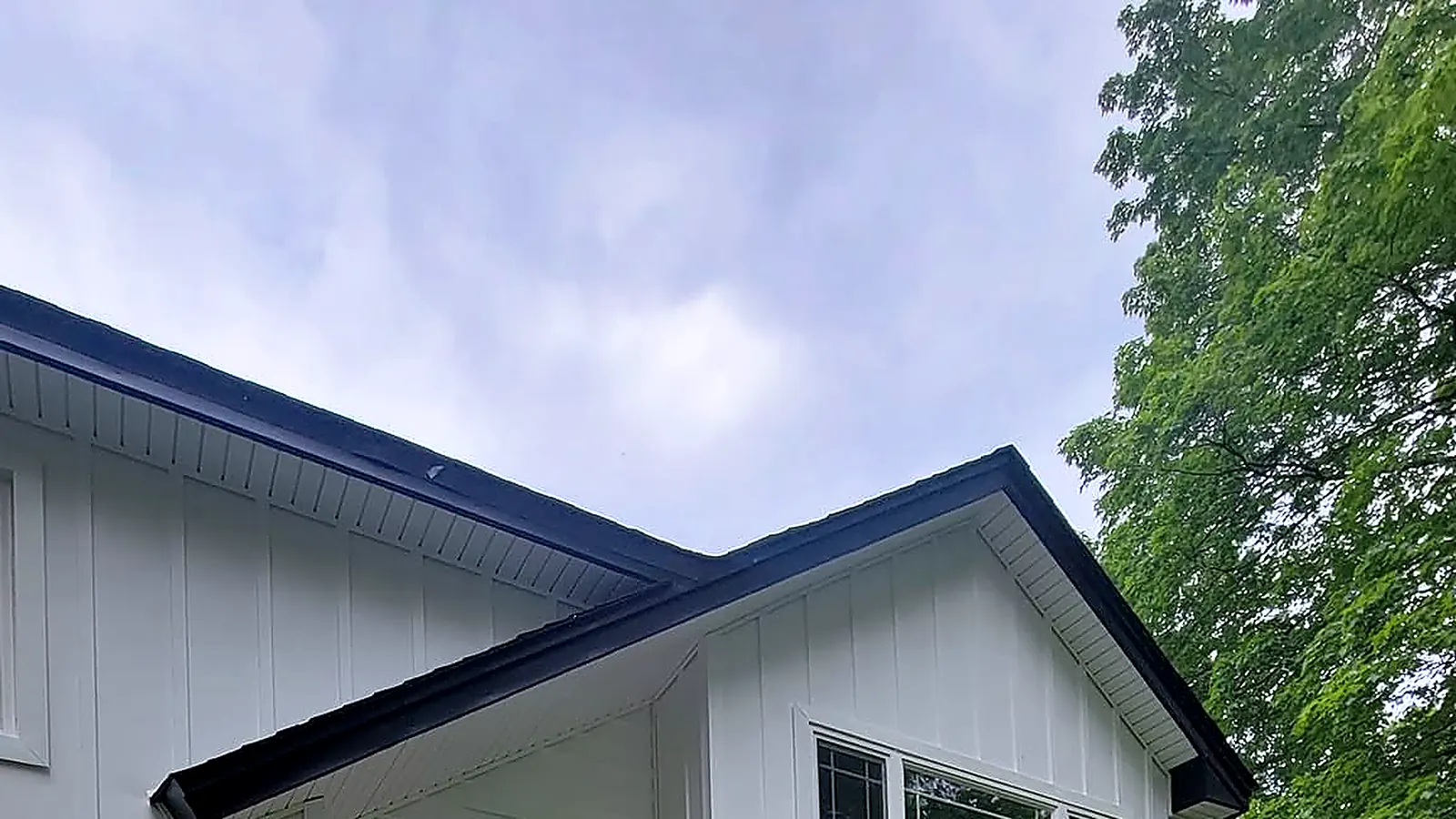 White board and batten siding on a gable with black roof trim and a dark barn light over the entry