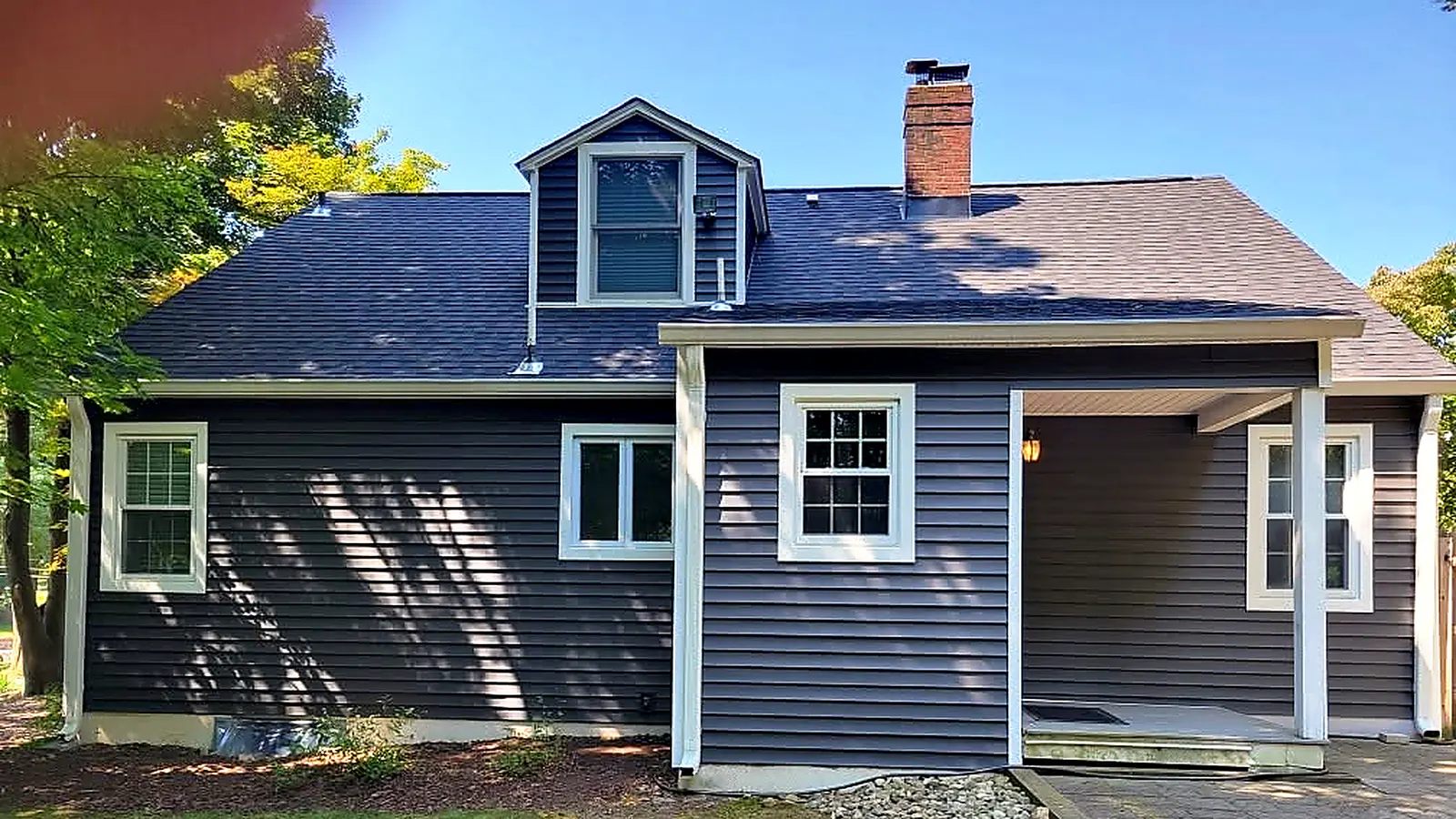 Rear of a navy-sided cape with a new dark shingle roof, a shed dormer and white-trimmed windows