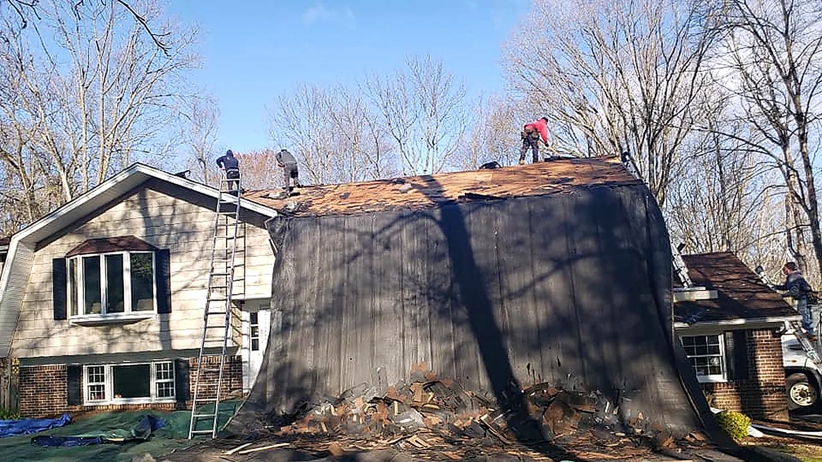 Roof tear-off underway on a North Jersey house with black tarps protecting the lawn and a crew on the roof