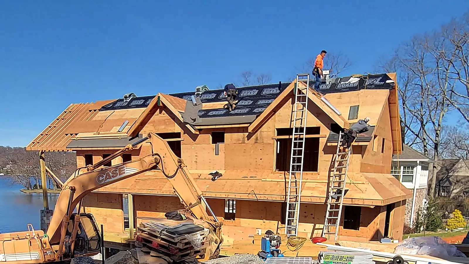 RJ Construction crew laying underlayment on the roof of a new lakefront house under construction