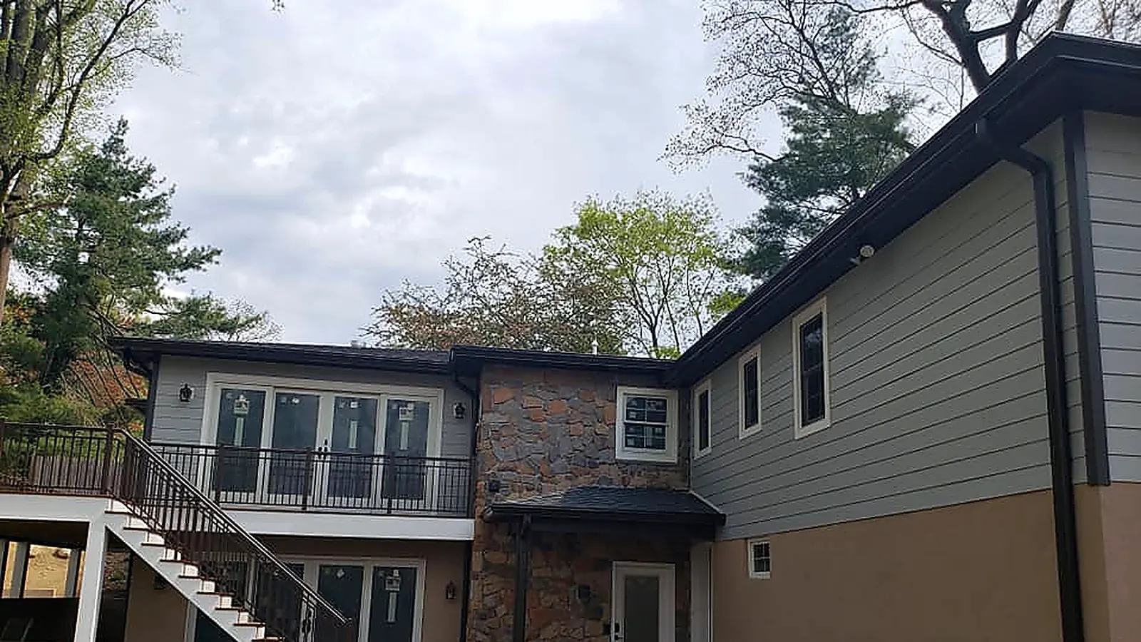 House with new gray lap siding, a stone-faced section, dark seamless gutters and a rear deck with metal railings