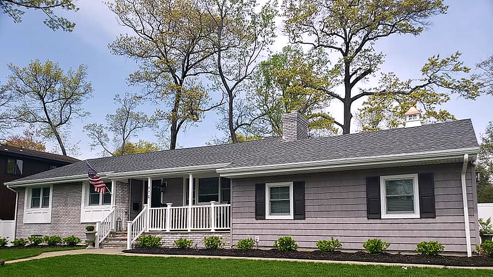 Ranch house with a new gray shingle roof, gray shake siding, a white porch railing and black shutters