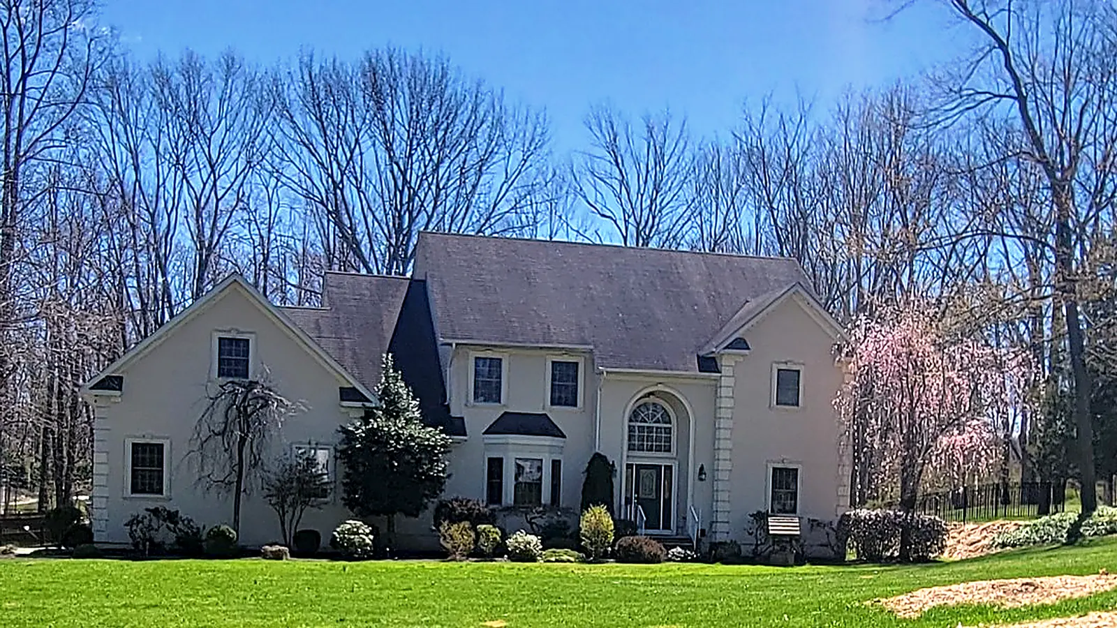 Large stucco colonial with a dark shingle roof and a flowering cherry tree in spring