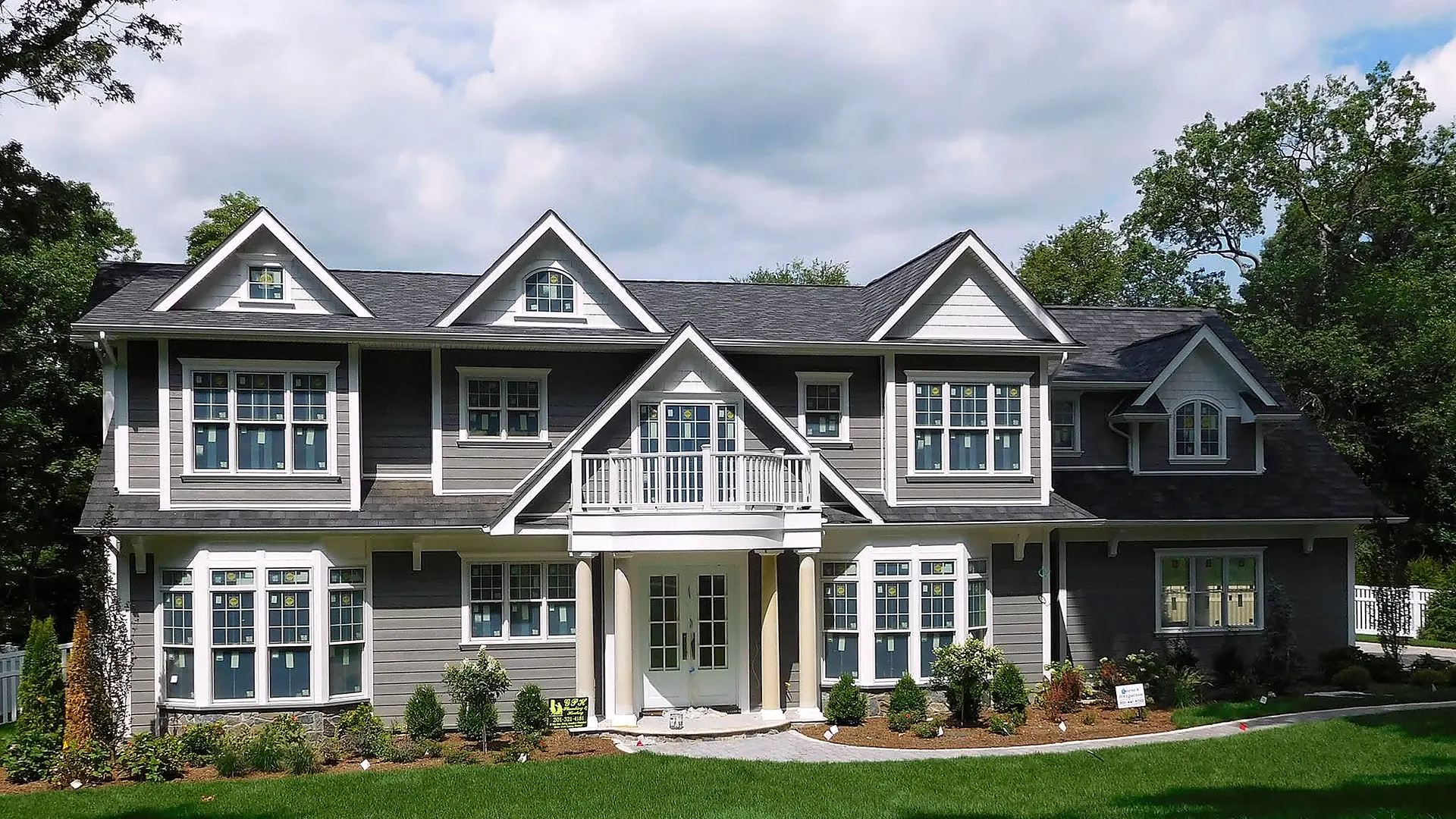 Large gray shingle-style colonial with a new dark asphalt shingle roof and white trim