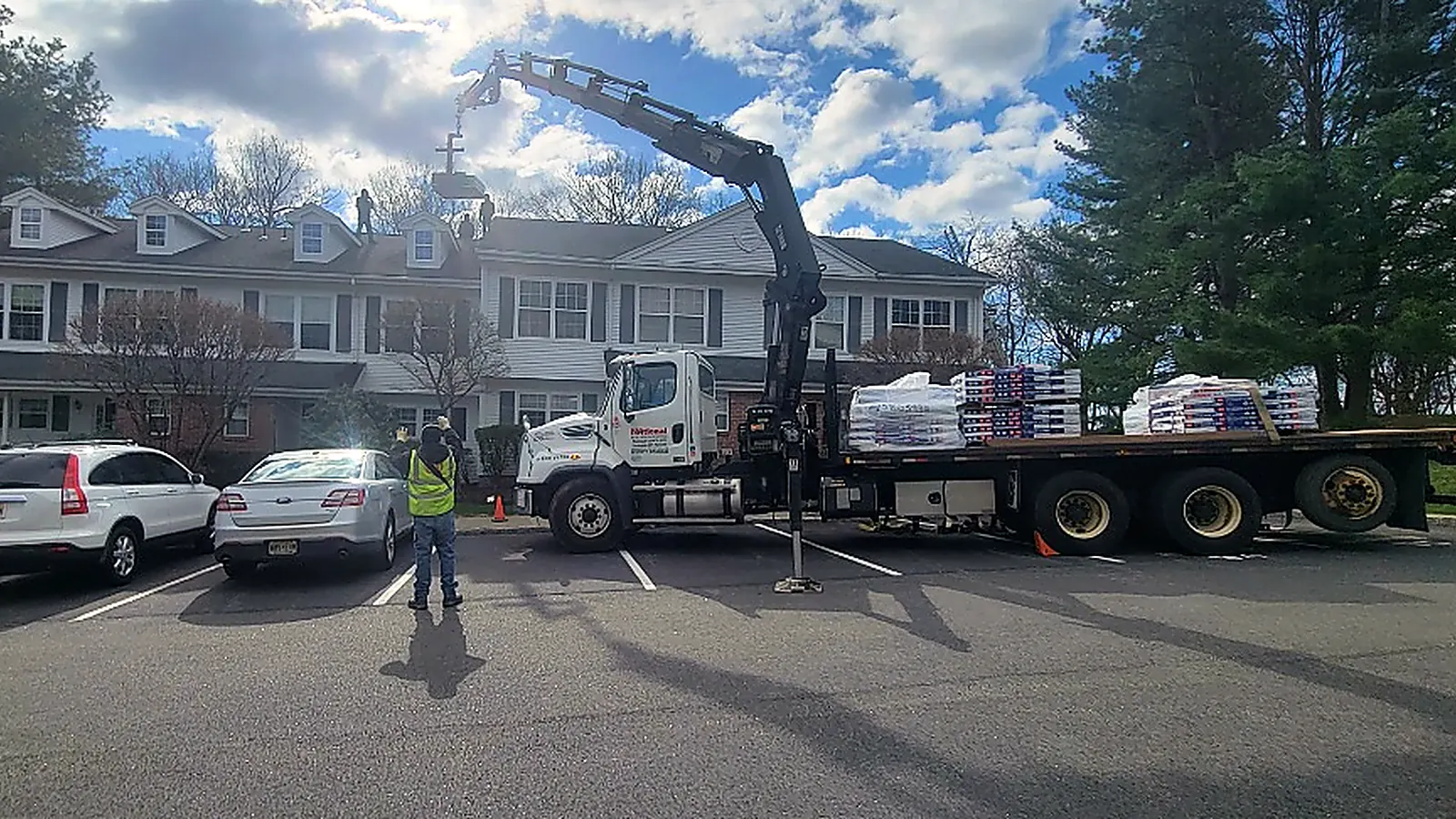Crane truck setting pallets of roofing materials onto a townhouse complex roof while a crew works
