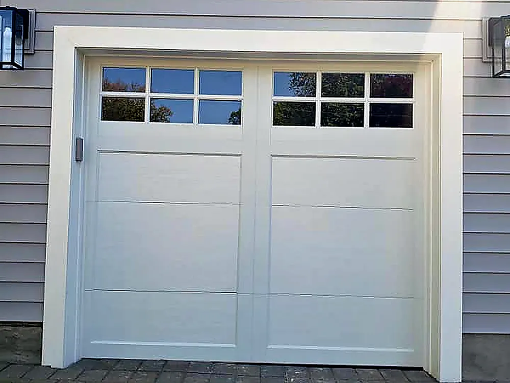 New white carriage-style garage door with a row of window lites, set in gray siding with lanterns on each side