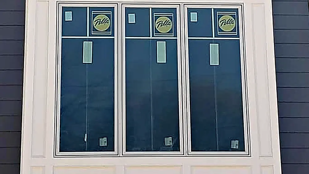New three-part window with the manufacturer labels still on the glass, installed in gray siding